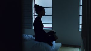 purpose of meditation helping woman meditating in dark bedroom to relax
